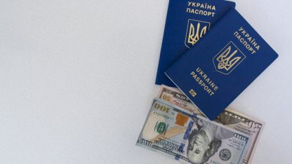Dois passaportes azuis da Ucrânia sobrepostos a notas de dólares americanos em um fundo branco. — Foto: Borys Zaitsev