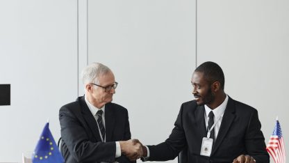 Dois homens de terno apertando as mãos em uma mesa com as bandeiras da União Europeia e dos Estados Unidos. — Foto: Werner Pfennig