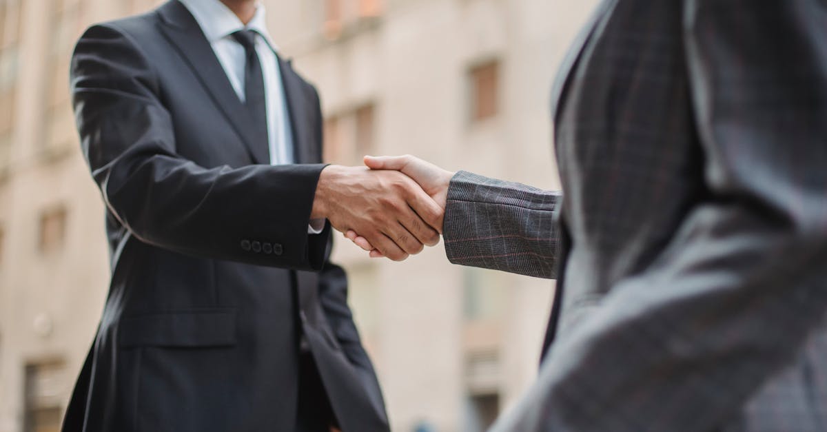 Dois profissionais em trajes formais de negócios apertando as mãos em frente a um edifício comercial. — Foto: Ketut Subiyanto