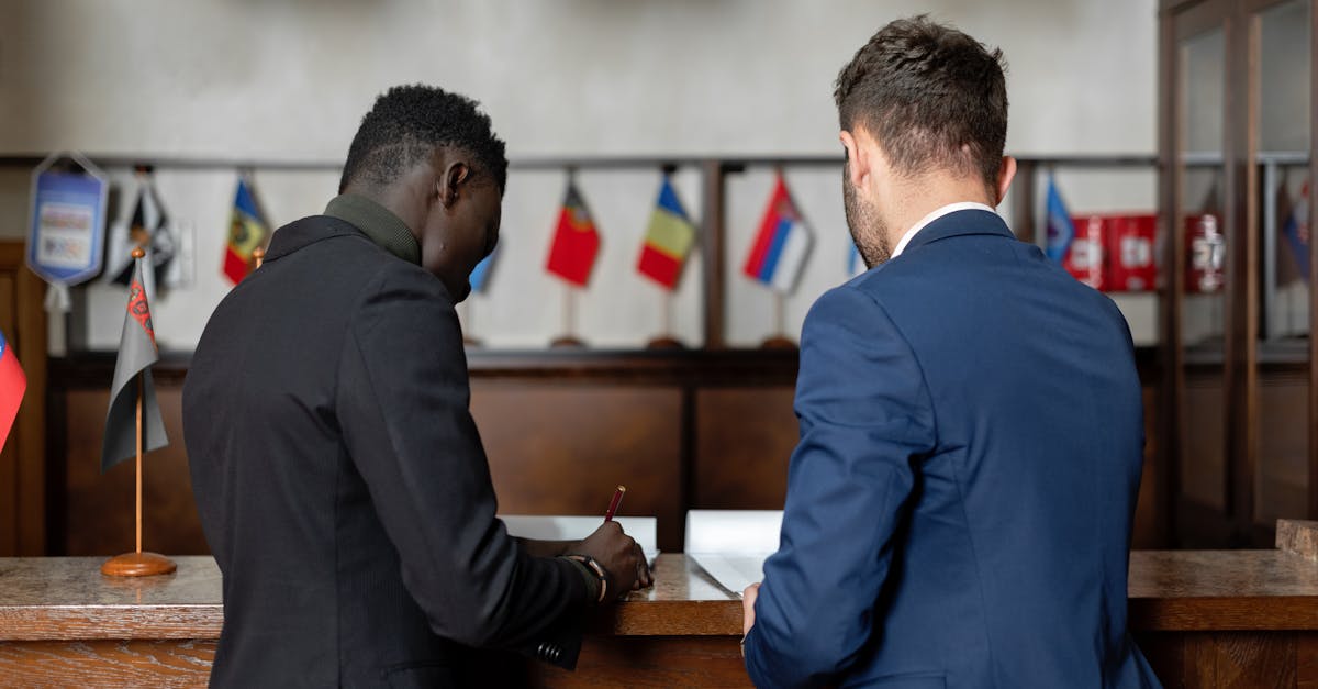 Dois homens de terno assinando documentos em um balcão de madeira com pequenas bandeiras de diversos países ao fundo. — Foto: Mikhail Nilov
