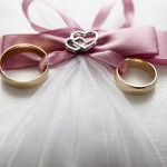 Duas alianças de ouro sobre uma almofada branca com laço rosa e detalhes em formato de coração. — Foto: Pixabay