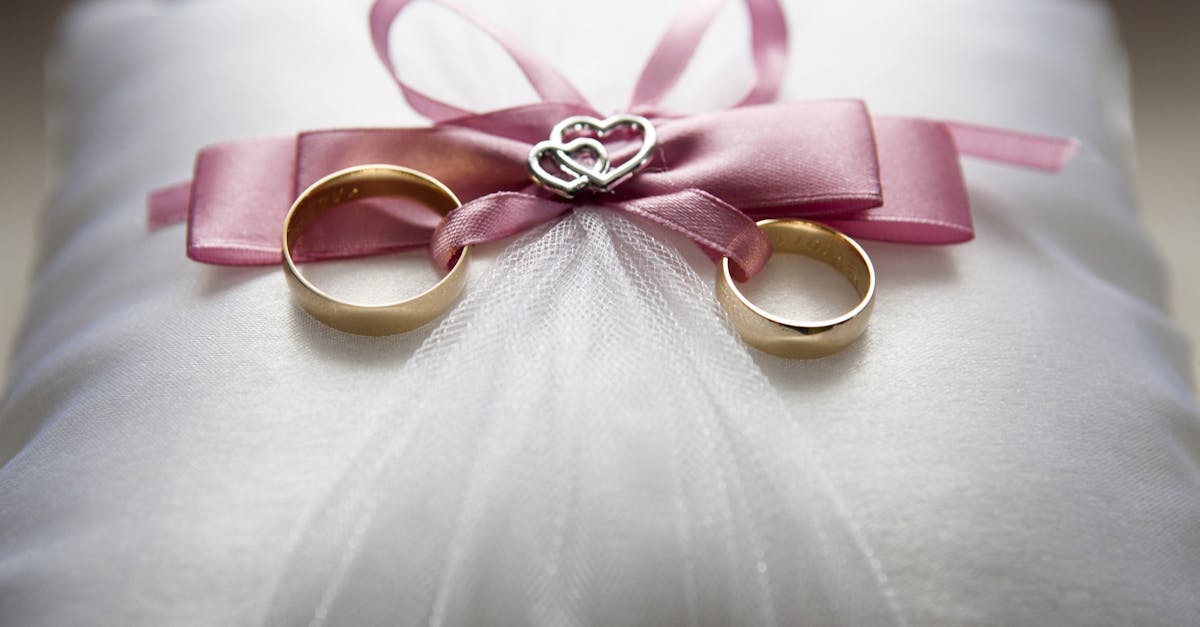 Duas alianças de ouro sobre uma almofada branca com laço rosa e detalhes em formato de coração. — Foto: Pixabay