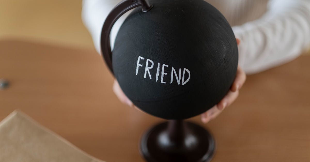 Mãos segurando um globo terrestre preto com a palavra FRIEND escrita em branco sobre uma mesa de madeira. — Foto: cottonbro studio