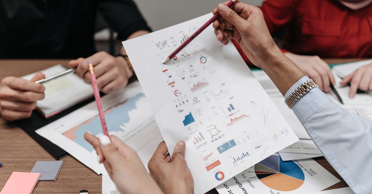 Pessoas em uma reunião de negócios analisando papéis com gráficos financeiros e tabelas sobre uma mesa de madeira. — Foto: Pavel Danilyuk
