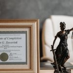 Estátua da deusa Têmis e certificado emoldurado sobre mesa de escritório de advocacia com cadeira ao fundo. — Foto: Pavel Danilyuk
