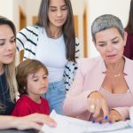 Uma advogada e uma família reunida em volta de uma mesa analisando documentos e plantas de imóveis. — Foto: Kampus Production