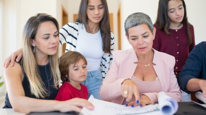 Uma advogada e uma família reunida em volta de uma mesa analisando documentos e plantas de imóveis. — Foto: Kampus Production