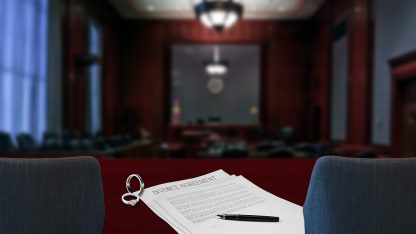 Documentos jurídicos com alianças e caneta sobre mesa em um tribunal desfocado ao fundo. — Foto: CFullerDesign