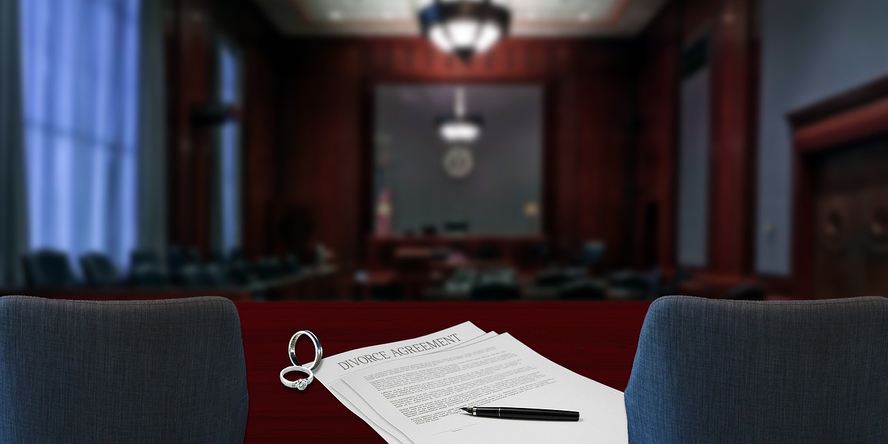 Documentos jurídicos com alianças e caneta sobre mesa em um tribunal desfocado ao fundo. — Foto: CFullerDesign