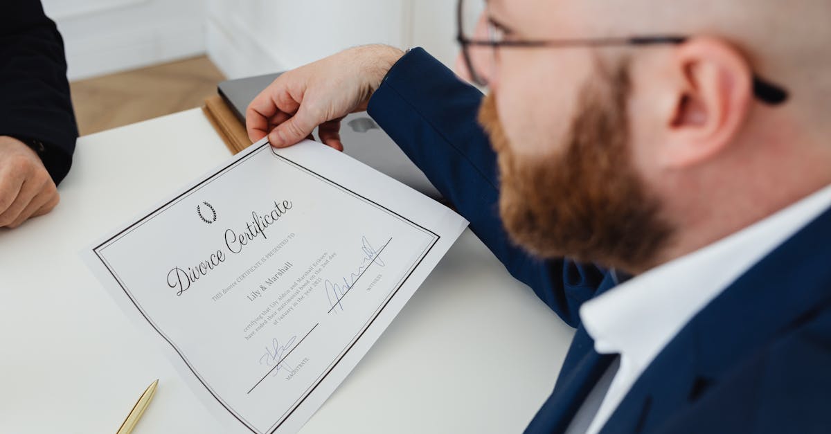 Homem de terno segurando um certificado de divórcio sobre uma mesa branca em um escritório. — Foto: www.kaboompics.com