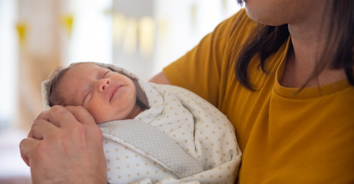 Pai segurando um bebê recém-nascido enrolado em uma manta branca com detalhes cinzas. — Foto: Kampus Production