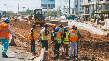 Grupo de operários com coletes reflexivos e capacetes trabalhando em uma obra urbana com maquinário pesado. — Foto: Yg pixel