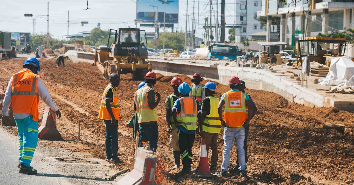 Grupo de operários com coletes reflexivos e capacetes trabalhando em uma obra urbana com maquinário pesado. — foto: yg pixel