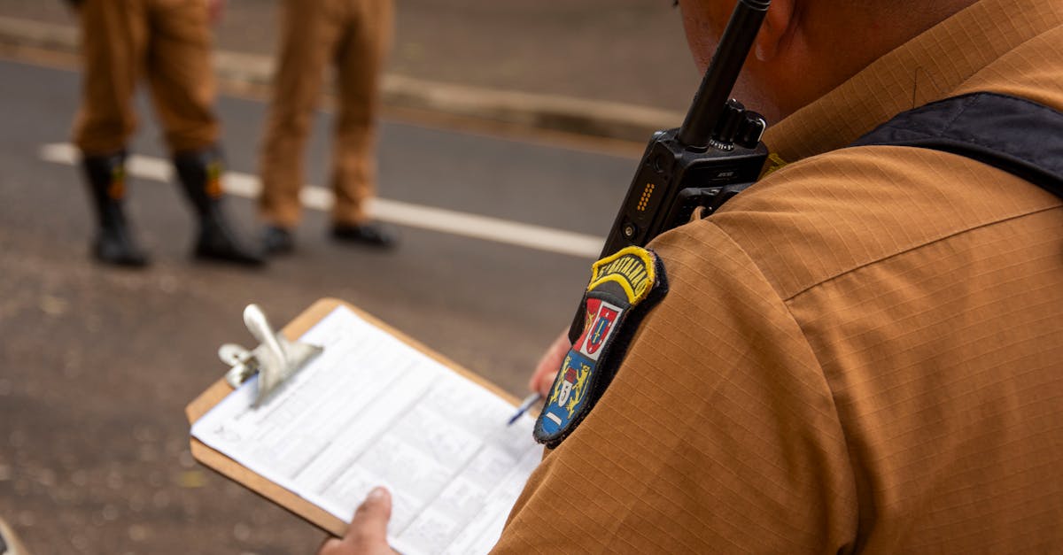 Agente uniformizado escrevendo em prancheta com rádio comunicador no ombro durante fiscalização externa. — Foto: Rodolfo Gaion
