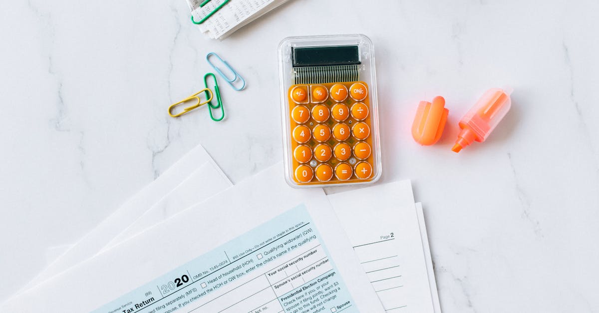 Vista superior de formulários de declaração de imposto, calculadora laranja, clipes e marcador sobre mesa branca. — Foto: Nataliya Vaitkevich