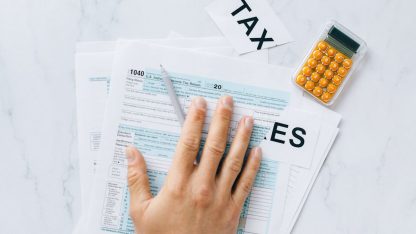 Mão sobre formulários de imposto de renda com calculadora e etiquetas escritas TAX ao lado. — Foto: Nataliya Vaitkevich
