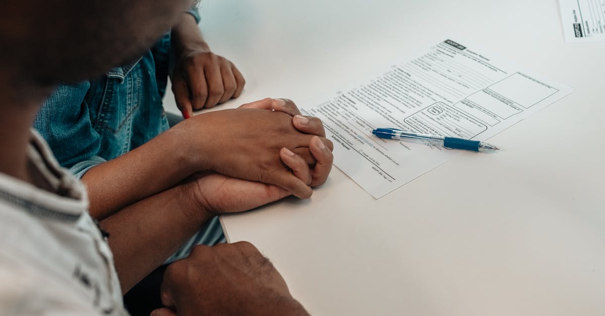 Duas pessoas com mãos dadas sobre uma mesa branca ao lado de um formulário impresso e uma caneta azul. — Foto: Kindel Media