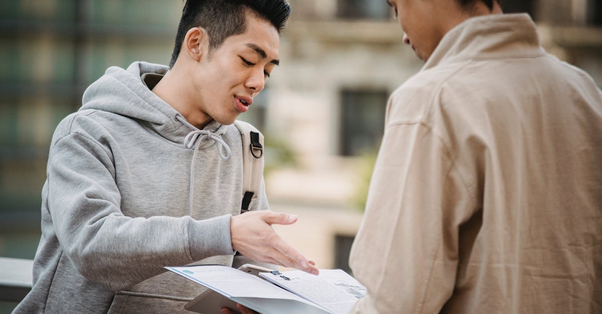 Jovem de moletom cinza gesticulando enquanto analisa documentos em uma prancheta com outra pessoa ao ar livre. — Foto: Armin Rimoldi