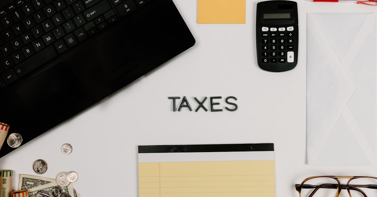 Vista superior de mesa com calculadora, teclado, moedas e a palavra TAXES centralizada em fundo branco. — Foto: Tara Winstead