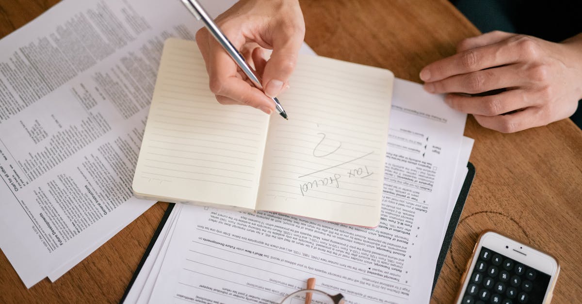 Pessoa escrevendo em caderno sobre mesa com documentos jurídicos e calculadora de celular. — Foto: Leeloo The First