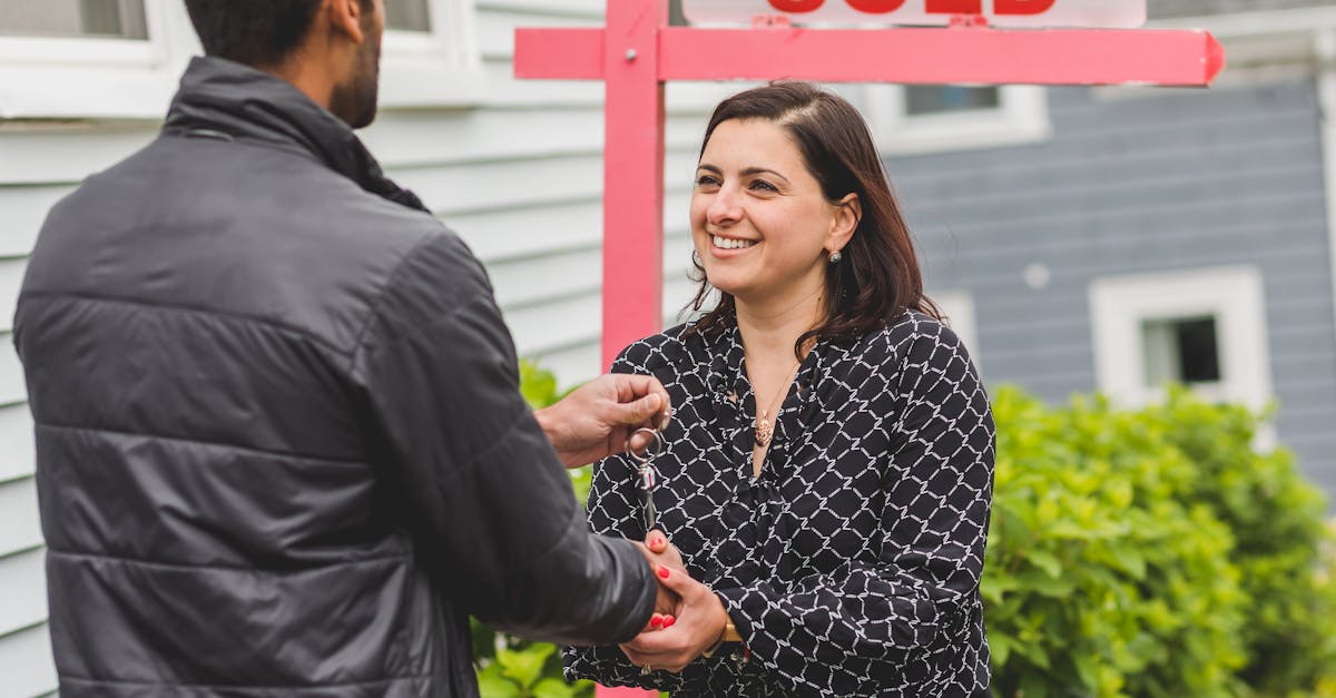 Mulher sorridente entregando as chaves de uma casa para um homem em frente a uma placa de venda. — Foto: RDNE Stock project