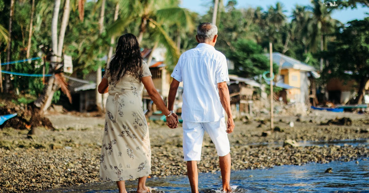 Casal de idosos caminhando de mãos dadas em uma praia tropical com palmeiras ao fundo. — Foto: Marc Majam