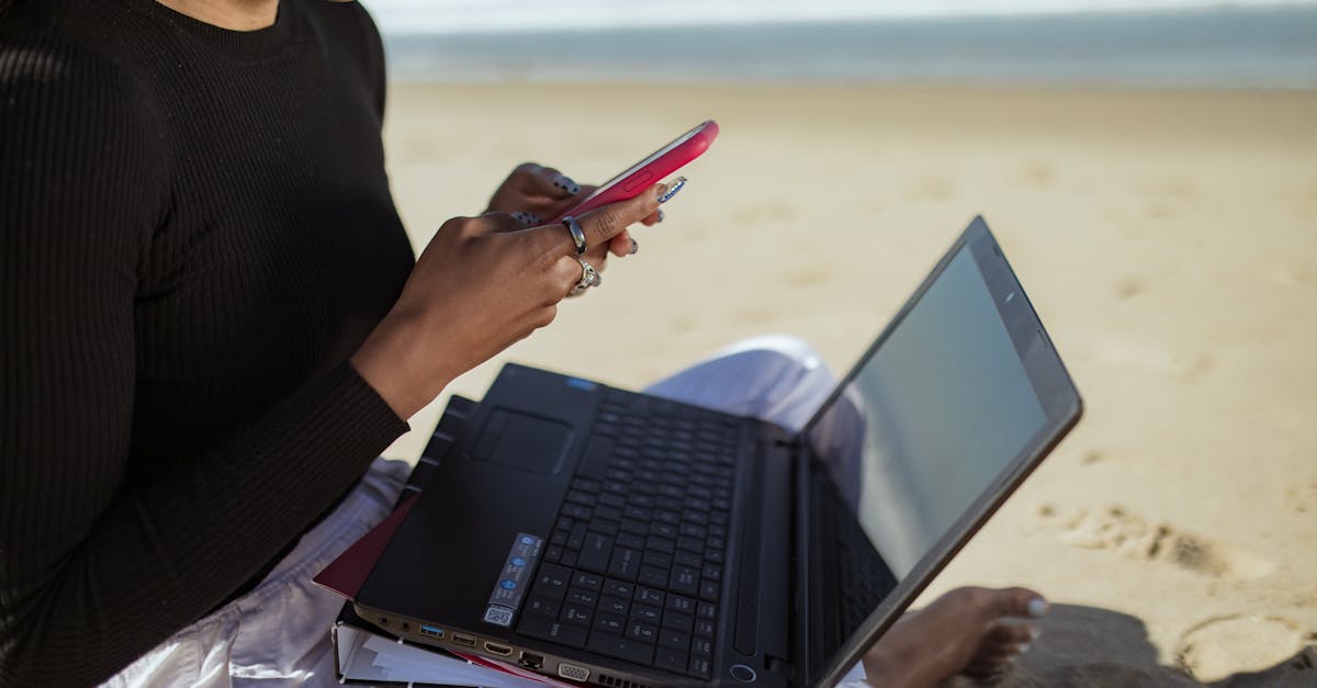 Pessoa sentada na areia da praia utilizando um notebook e segurando um celular, representando trabalho remoto. — Foto: RDNE Stock project