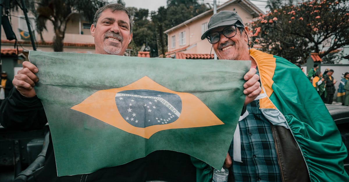 Dois homens sorridentes segurando a bandeira do Brasil em uma rua residencial. — Foto: Joel Santos