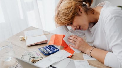 Mulher preocupada analisando contas, faturas e calculadora sobre uma mesa de escritório. — Foto: www.kaboompics.com
