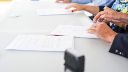 Pessoas sentadas à mesa assinando documentos e contratos com um carimbo em primeiro plano. — Foto: vmamic