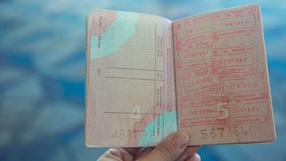 Visto para americanos canadenses e australianos em 2026 82802 1775267740 Mão segurando um passaporte aberto exibindo carimbos de imigração em páginas rosadas. — foto: ekaterina belinskaya