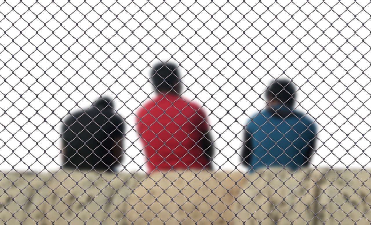 Asylum and refugee status brazil inline 1 135070 1779975360 Três pessoas vistas de costas atrás de uma cerca de arame, simbolizando fronteira e imigração. — foto: geralt