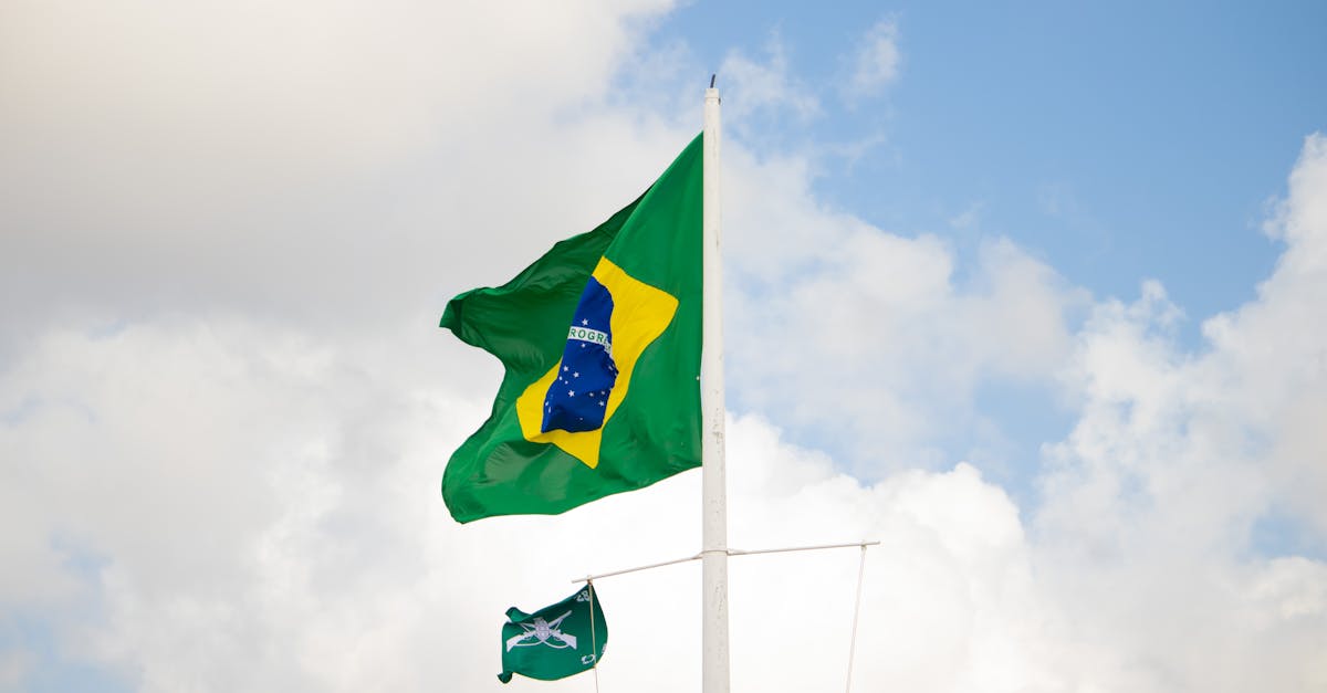 Bandeira do Brasil hasteada em um mastro sob um céu azul com nuvens brancas. — Foto: Tallita Maynara