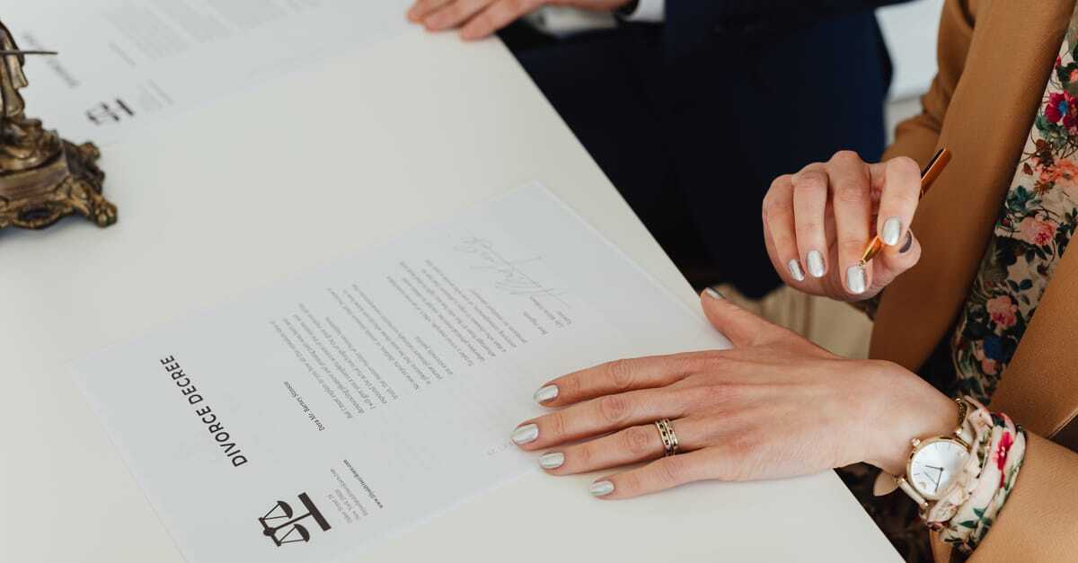Mulher assinando documentos em uma mesa com outro indivíduo, em um ambiente de escritório. — Foto: www.kaboompics.com