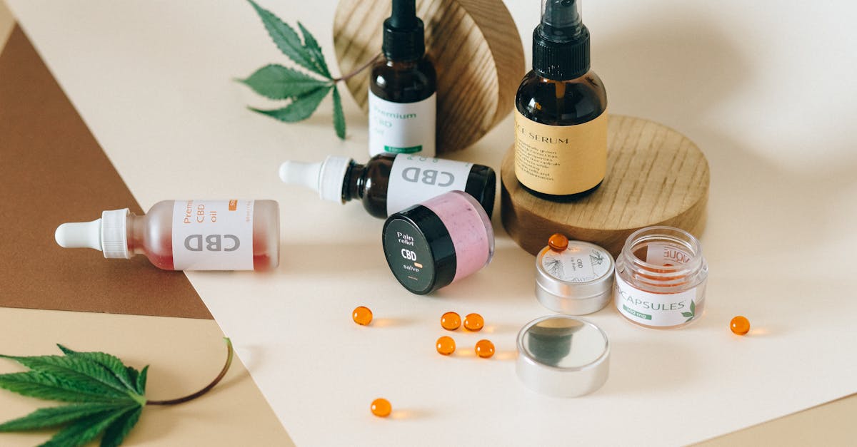 Frascos de óleo de CBD, cápsulas e potes de cosméticos dispostos sobre uma superfície clara com folhas de cannabis. — Foto: Nataliya Vaitkevich