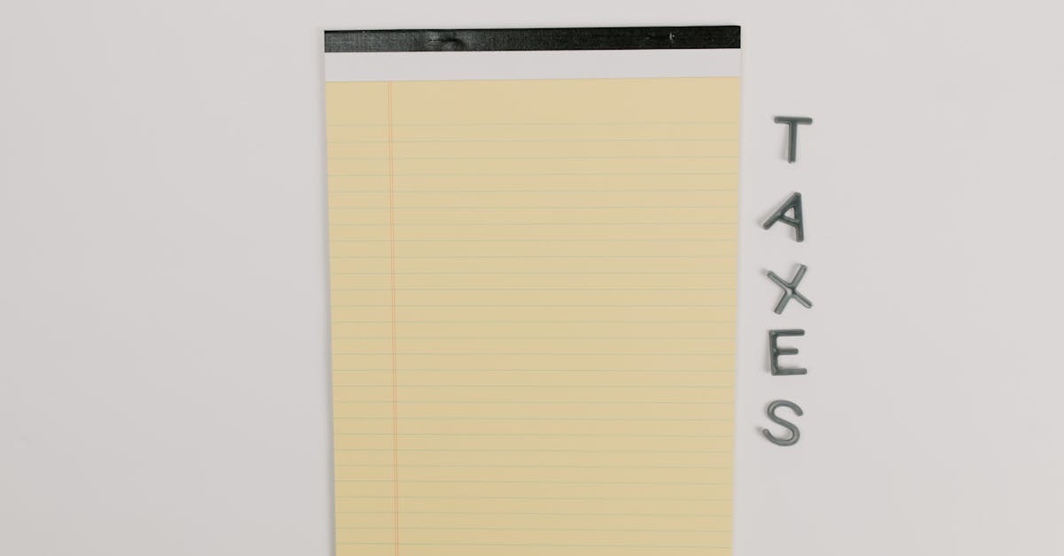 Bloco de notas amarelo ao lado da palavra 'TAXES' escrita em letras metálicas sobre fundo branco. — Foto: Tara Winstead