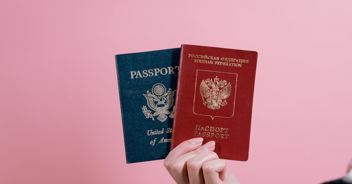 Mão segurando passaportes dos Estados Unidos e da Rússia contra fundo rosa. — Foto: Tima Miroshnichenko