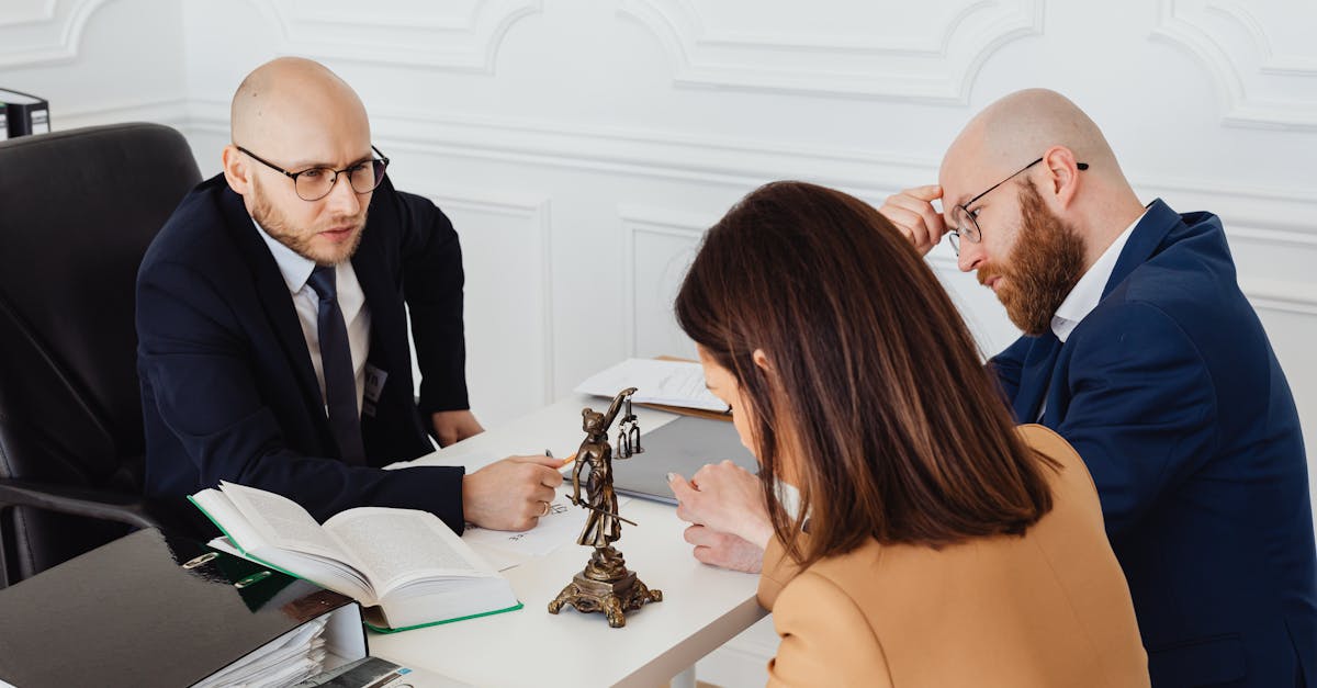 Advogados em reunião com cliente em escritório, com livros jurídicos e estátua da justiça sobre a mesa. — Foto: www.kaboompics.com