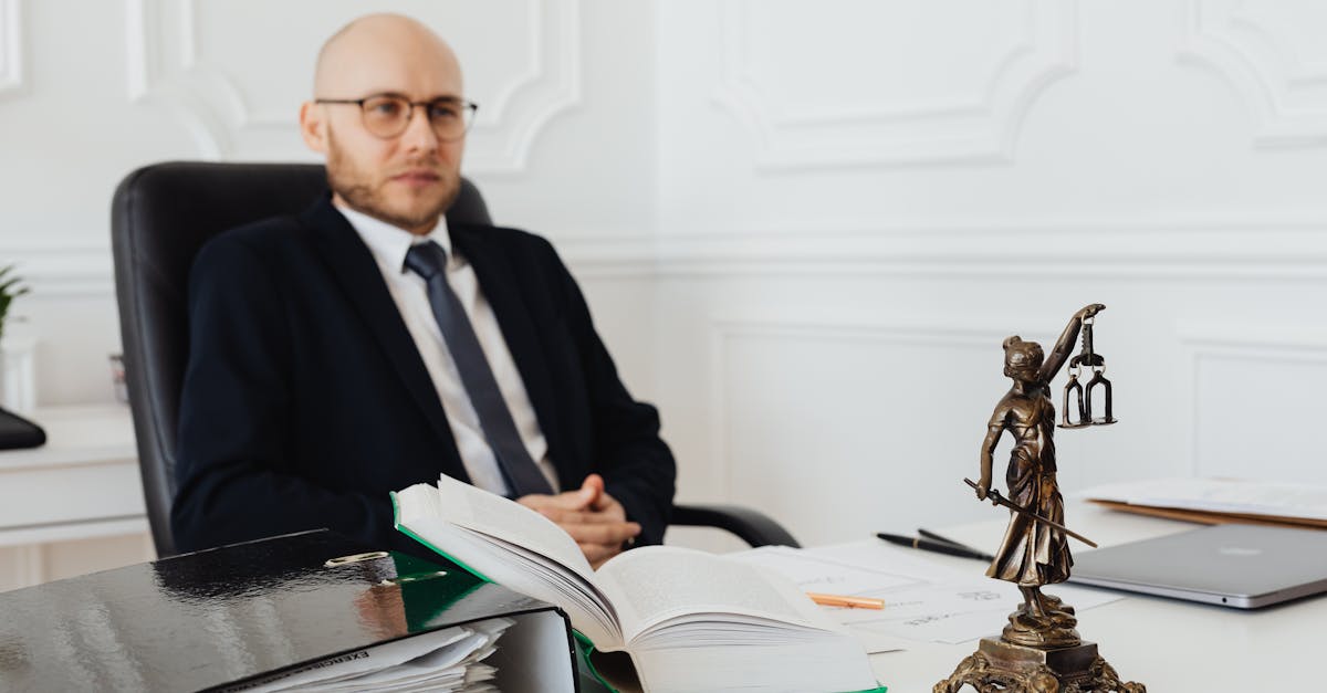 Advogado de terno sentado em sua mesa de escritório com uma estatueta da justiça ao lado. — Foto: www.kaboompics.com