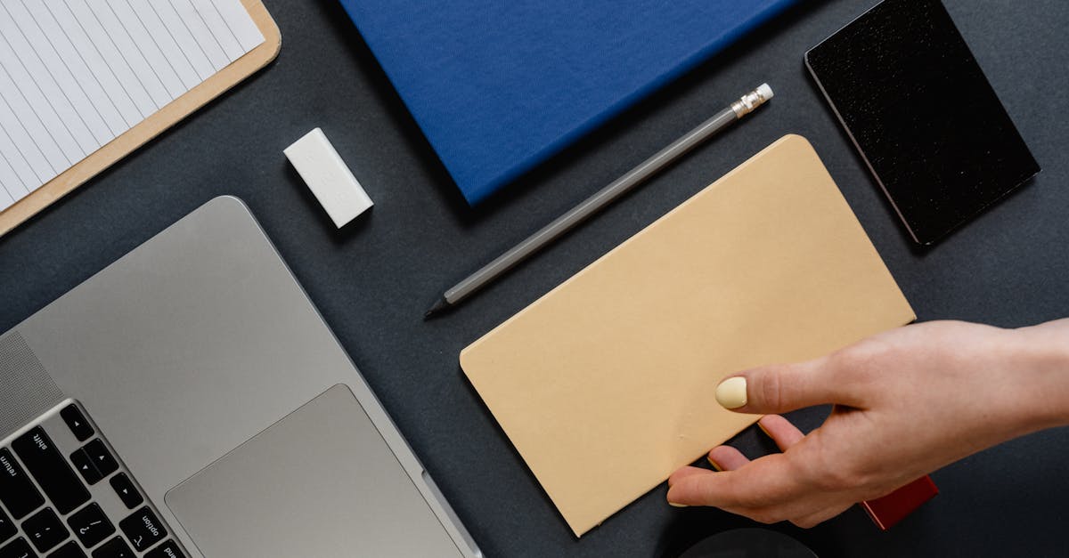 Mão sobre mesa de escritório com notebook, cadernos, lápis e smartphone. — Foto: MART PRODUCTION