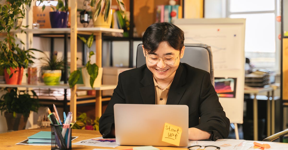 Homem de terno sorrindo enquanto trabalha em um notebook em um escritório moderno com plantas ao fundo. — Foto: ANTONI SHKRABA production