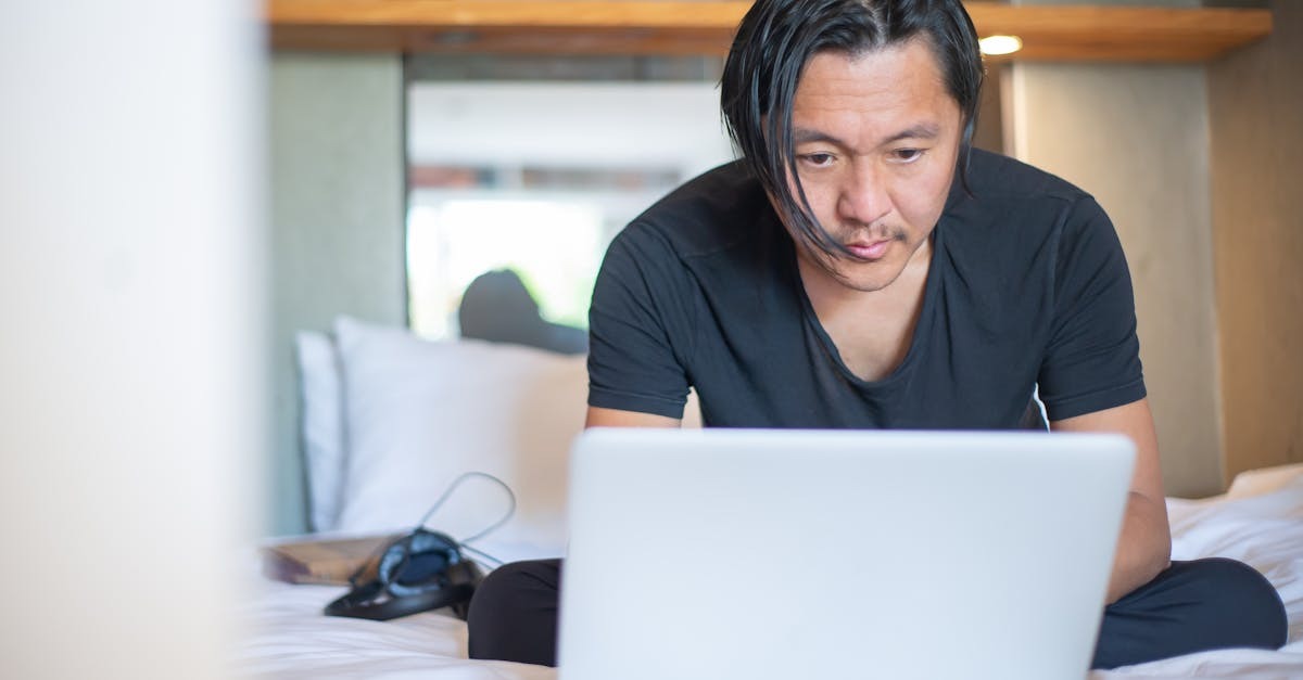 Homem usando laptop em cama de hotel, possivelmente trabalhando remotamente. — Foto: Kampus Production