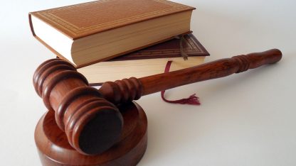 Martelo de madeira de juiz apoiado sobre base ao lado de dois livros jurídicos de capa dura. — Foto: succo
