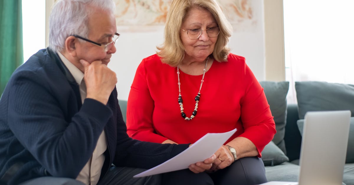 Casal de idosos sentados em um sofá analisando papéis e documentos com um notebook à frente. — Foto: Kampus Production