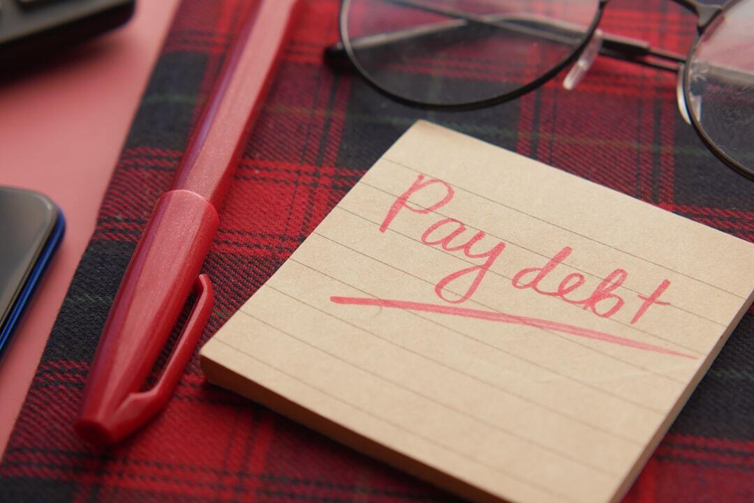 Bloco de notas com 'Pay debt' e caneta, sugerindo organização financeira pessoal. — Foto: Towfiqu barbhuiya