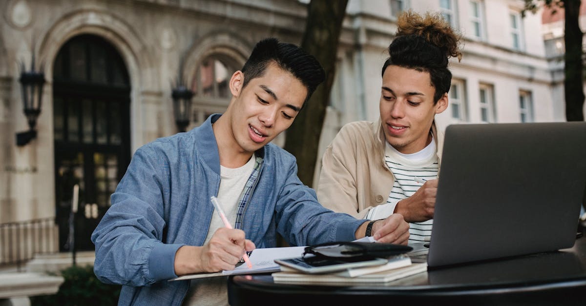 Dois jovens sentados em uma mesa ao ar livre, um deles escrevendo em documentos e o outro olhando para um laptop. — Foto: Armin Rimoldi