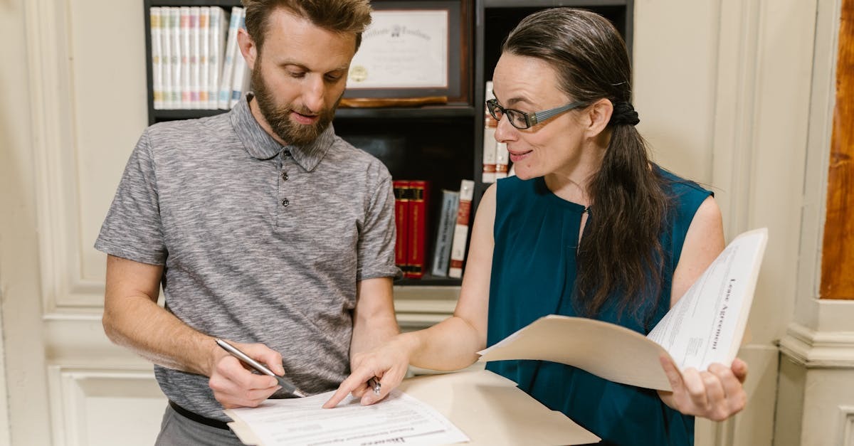 Mulher de óculos orientando um homem que assina documentos em um escritório. — Foto: RDNE Stock project