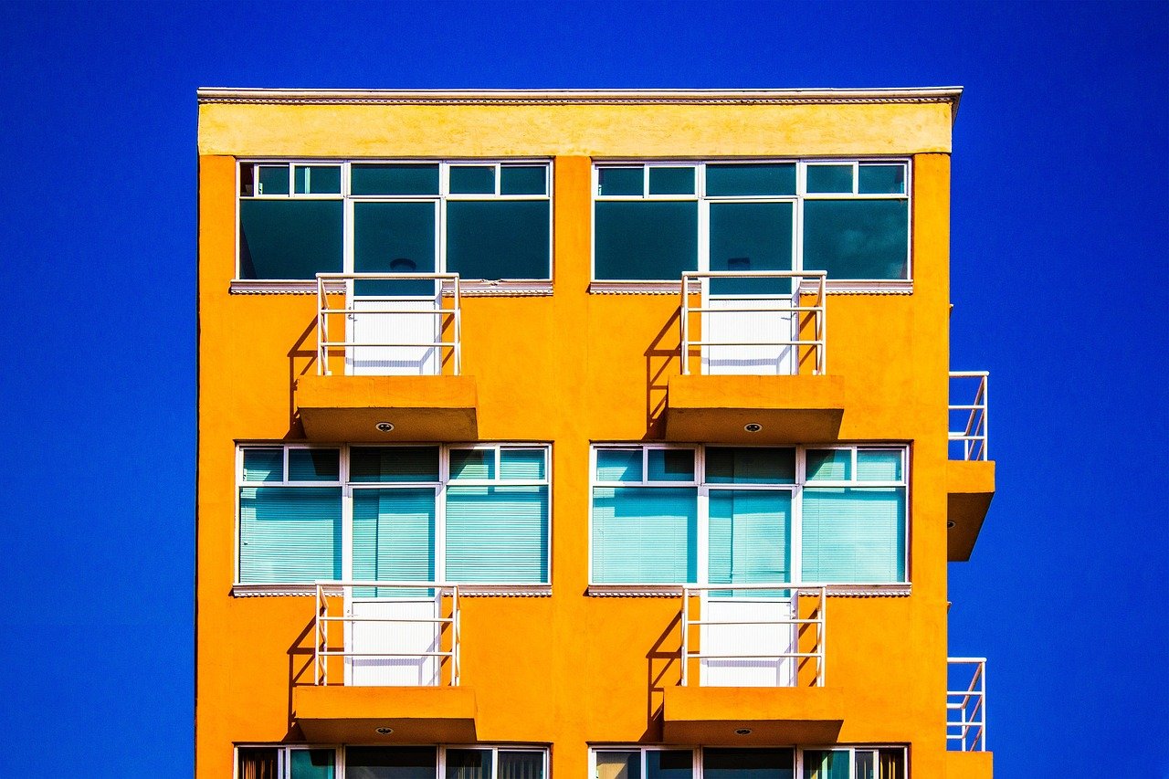 Fachada de prédio residencial amarelo com sacadas sob céu azul intenso. — Foto: rotekirsche20