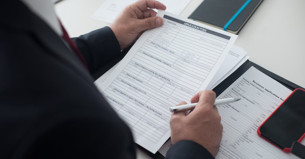 Pessoa de terno segurando e analisando documentos e formulários em uma mesa de escritório. — Foto: Kampus Production