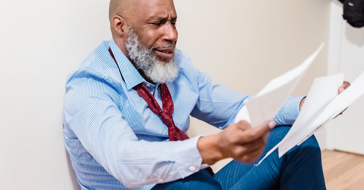 Homem idoso de camisa e gravata sentado no chão, com expressão preocupada enquanto analisa documentos financeiros. — Foto: Nicola Barts
